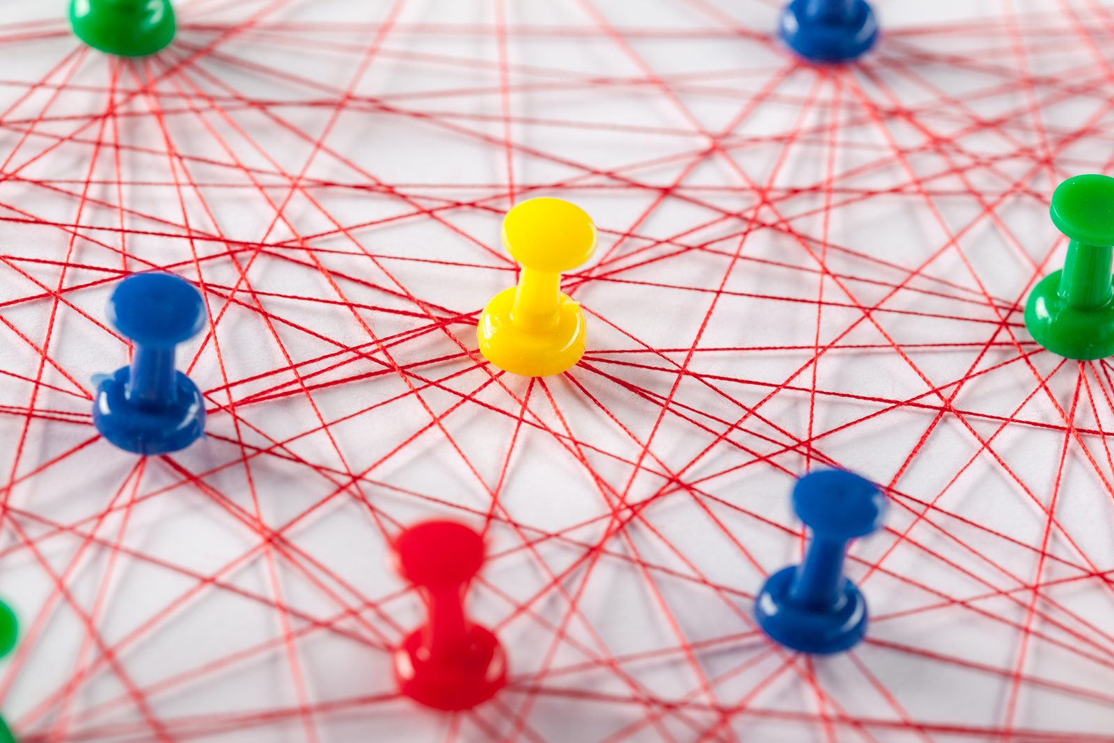 Colorful pushpins connected by red strings on whit
