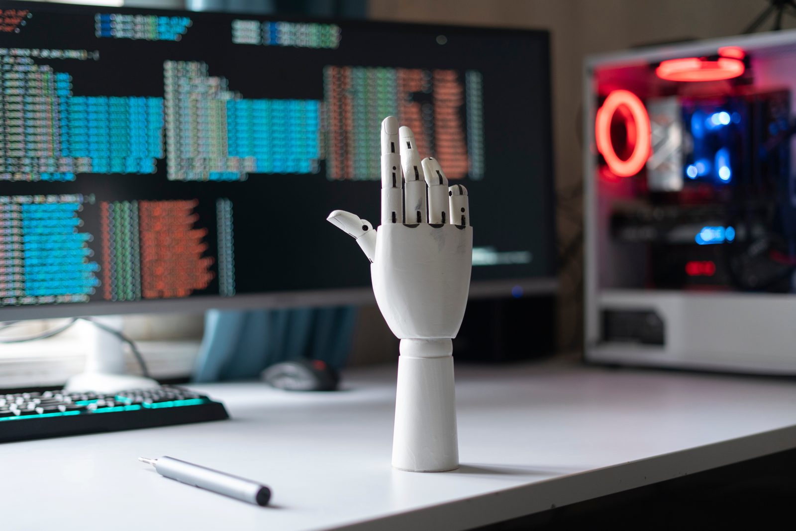 A wooden mannequin hand at a desk in front of monitors full of code